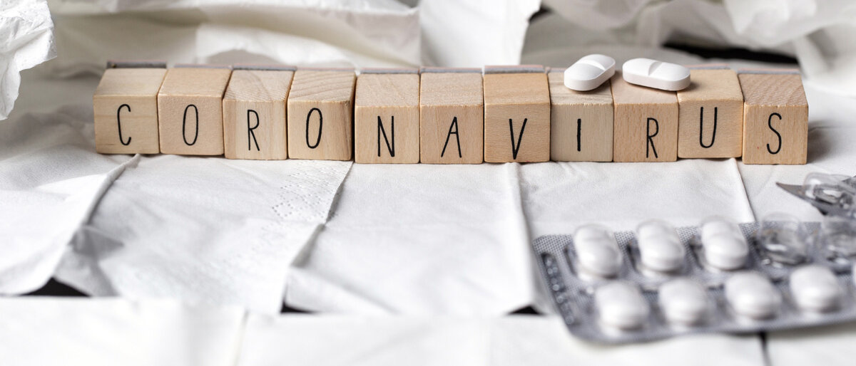 Das Wort Coronavirus in Holzwürfeln gelegt, im Hintergrund Taschentücher und Tablettenblister