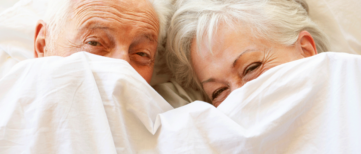 Zwei Senioren unter einer Bettdecke, Gesichter halb bedeckt