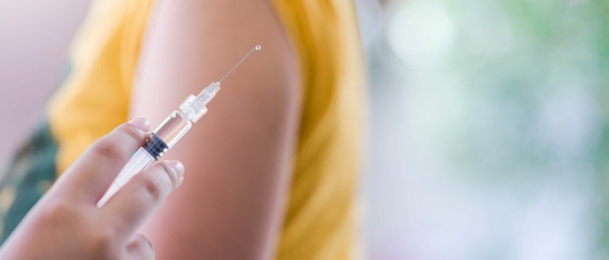 Nahaufnahme einer Spritze vor einem Arm.