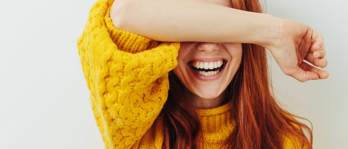 Lächeln Eine Frau lächelt offen und verdeckt dabei ihre Augen mit dem Arm.