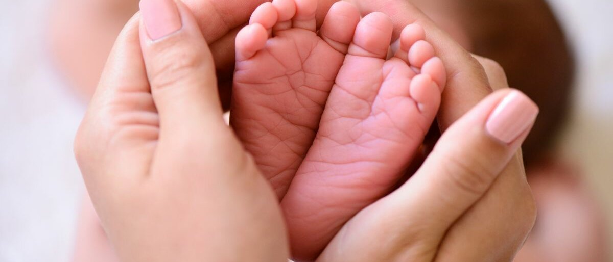 Frauenhände halten Babyfüße.