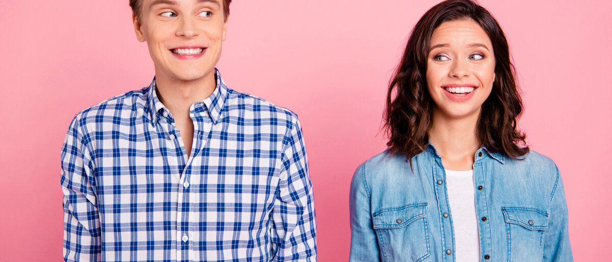 Ein junges Paar lächelt sich skeptisch an.