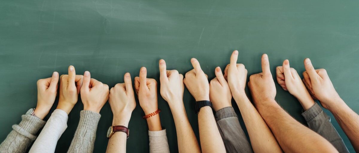 Daumen Zwölf Arme vor einer Tafel, die Daumen hoch zeigen.