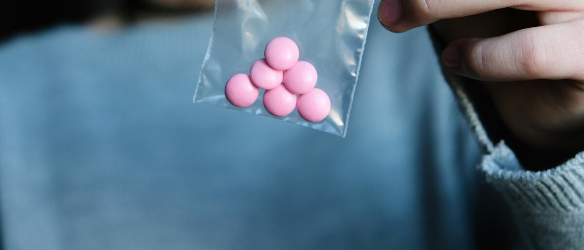 Jemand hält ein durchsichtiges Tütchen mit rosa Pillen hoch