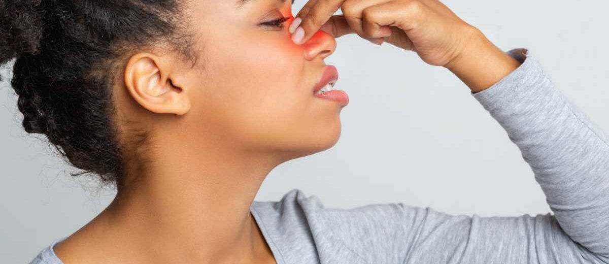 Rhinosinusitis Eine Frau fasst sich an die Nase. Ihre Rhinosinusitis ist rot angedeutet.