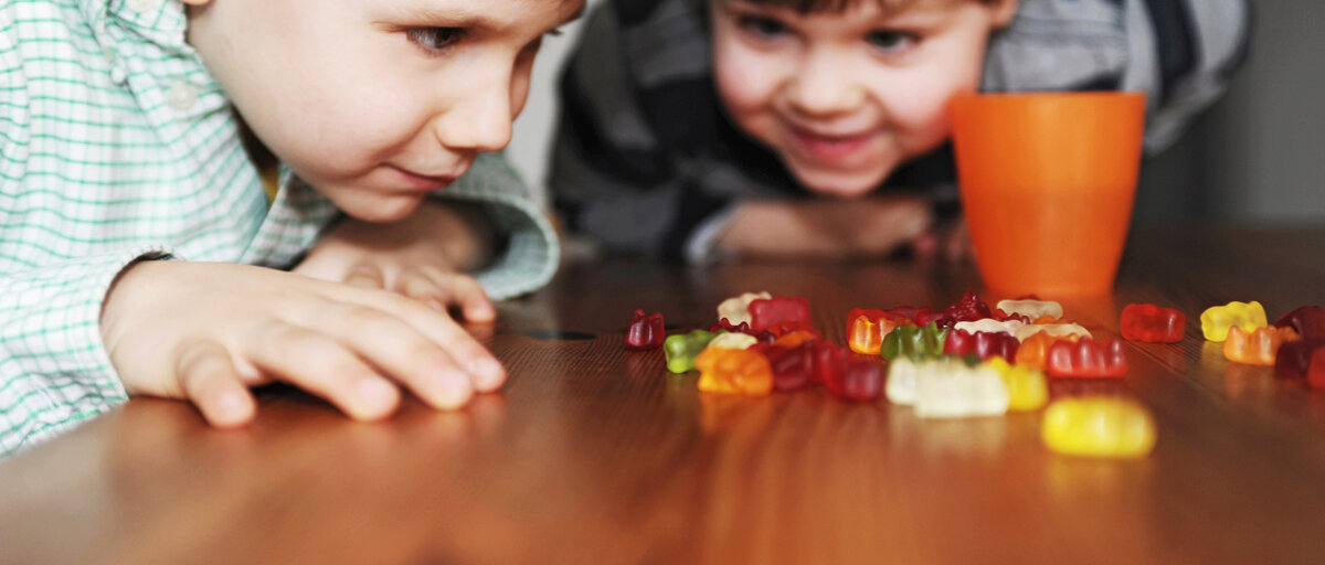 Zwei Jungen im Grundschulalter sitzen an einem Tisch und teilen Gummibärchen zwischen sich auf.
