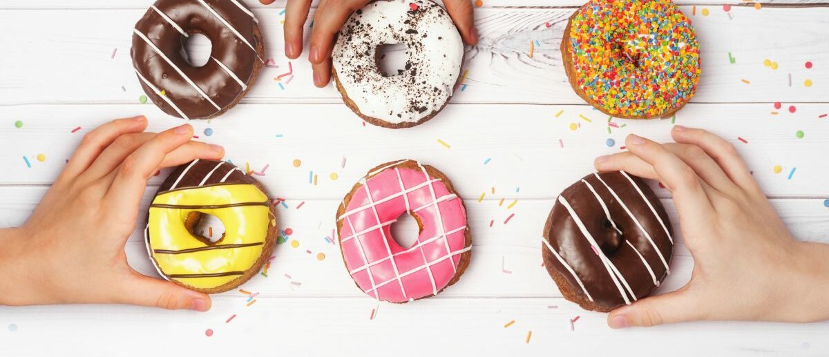 Donuts auf einem weißen Tisch und Kinderhände, die sich die Donuts greifen wollen.