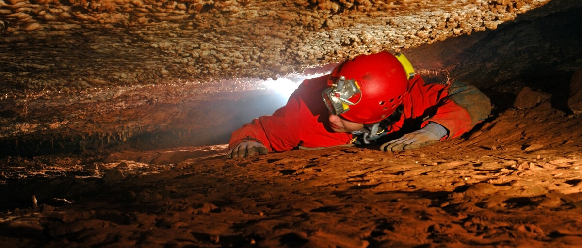 Ein Höhlenkletterer zwengt sich durch eine enge Stelle.