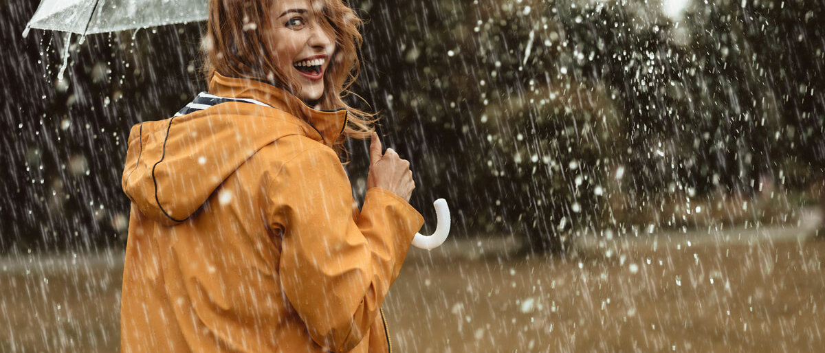 eine lachende Frau unter einem Schirm im Regen