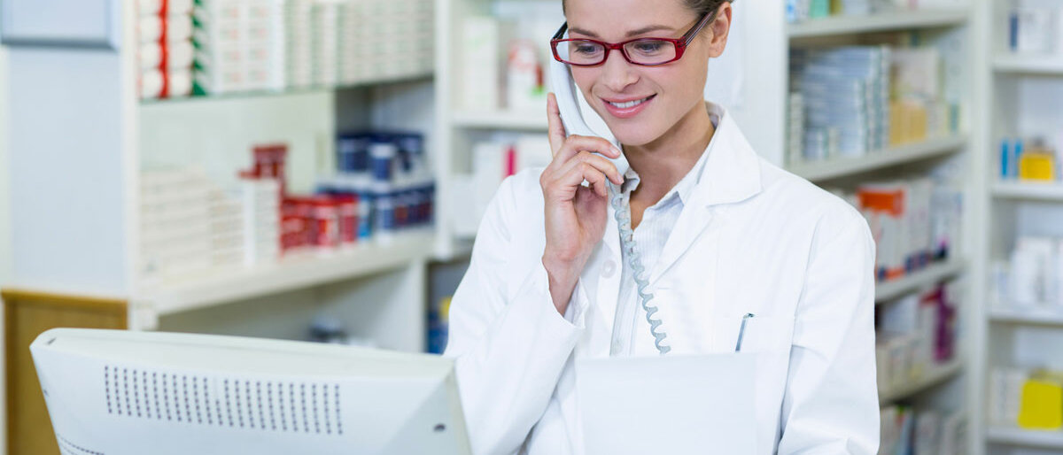 Eine Apothekenmitarbeiterin schaut in den Computer und telefoniert.