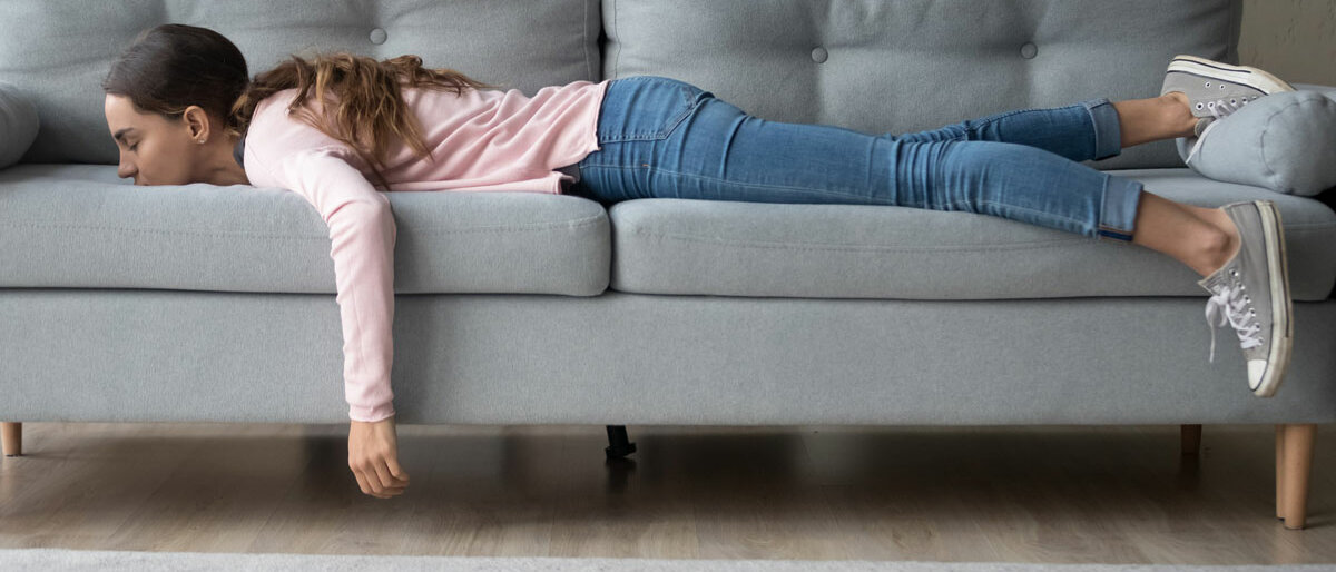 Eine junge Frau liegt vollständig bekleidet und mit Schuhen bäuchlings ausgestreckt auf dem Sofa.