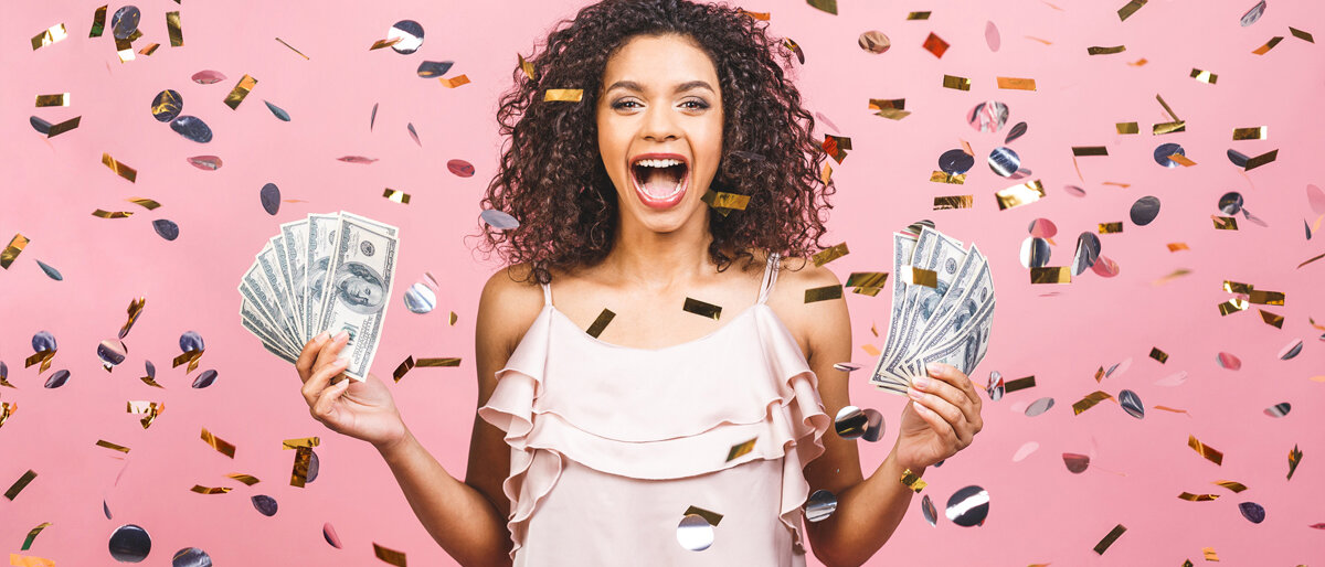Eine Frau hält Fächer in beiden Händen aufgefächerte Geldscheine, reißt den Mund vor Freude auf und steht im Konfettiregen.