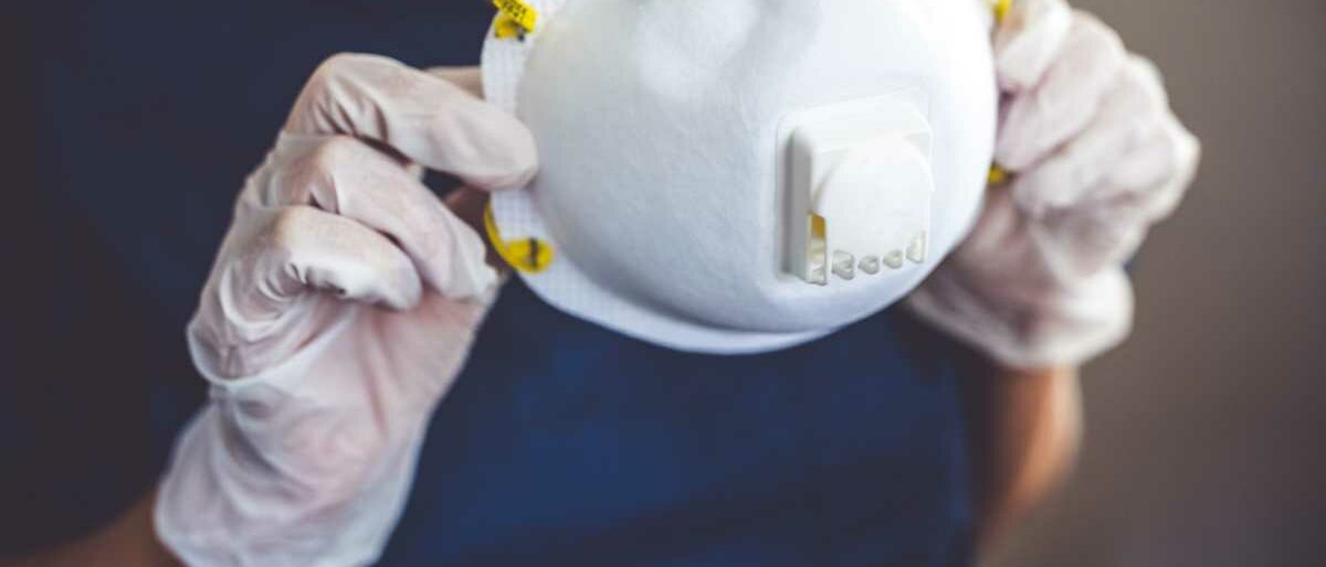 Eine Ärztin in blauem Kasack hält eine FFP2-Maske.