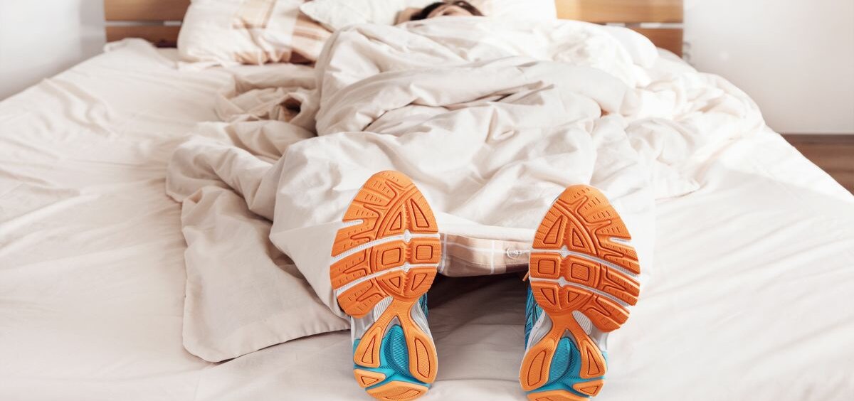 Pause Jemand liegt zugedeckt mit Sportschuhen im Bett.
