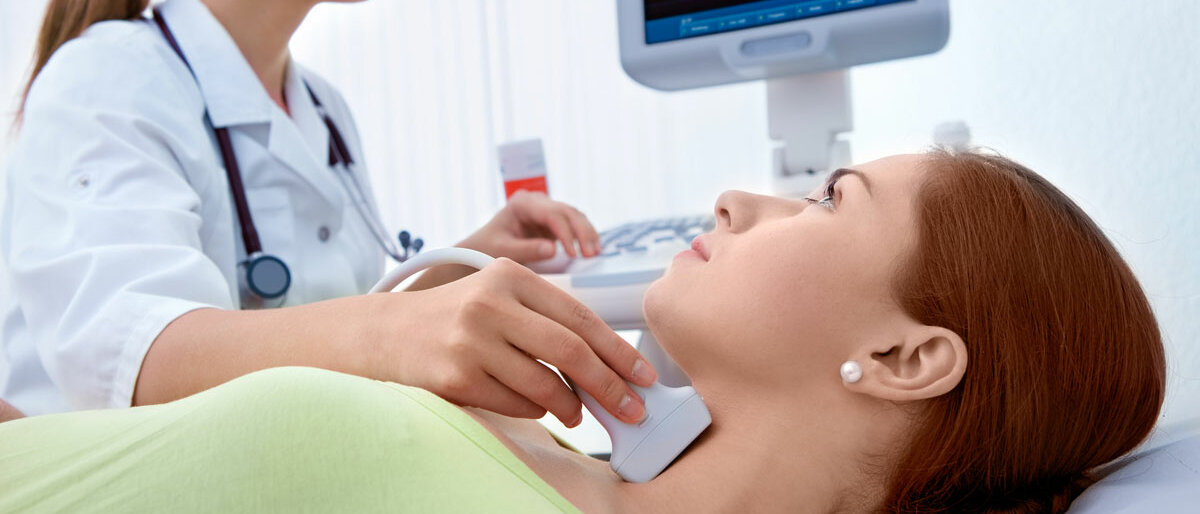 Eine Frau liegt auf einer Behandlungsliege, eine Ärztin untersucht ihren Hals mittels Ultraschall.