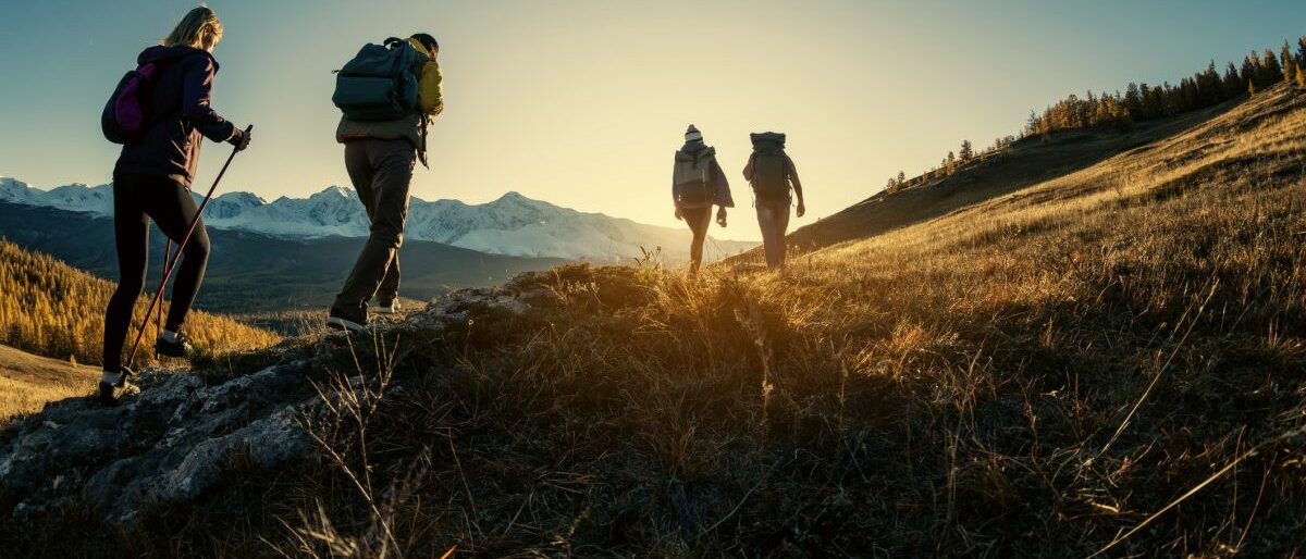 Vier Menschen wandern während des Sonnenuntergangs durch eine Berglandschaft.