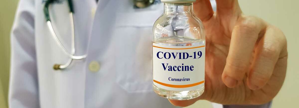 Ein Arzt hält eine Impf-Phiole hoch, die die Aufschrift "Covid-19 Vaccine" trägt.