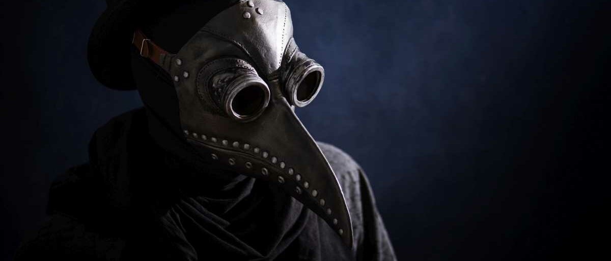Eine dunkel gekleidete Gestalt trägt eine mittelalterliche Pestmaske und Zylinder.