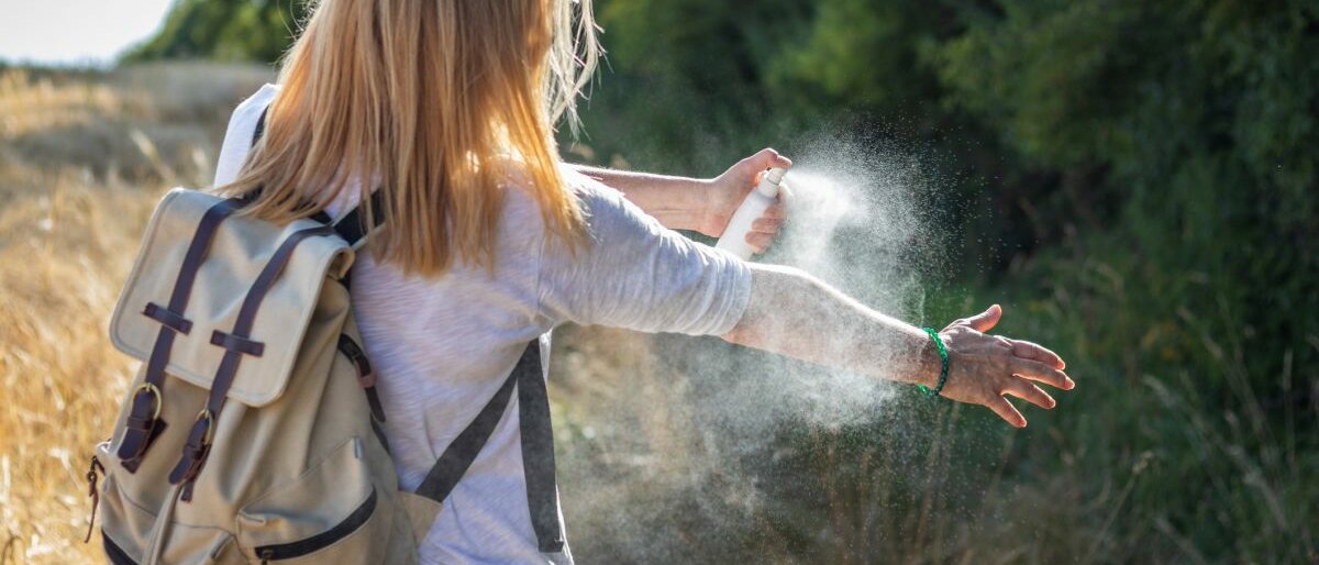 Insektenabwehr Eine Frau sprüht ihren Arm mit einem Insektenabwehrspray ein.
