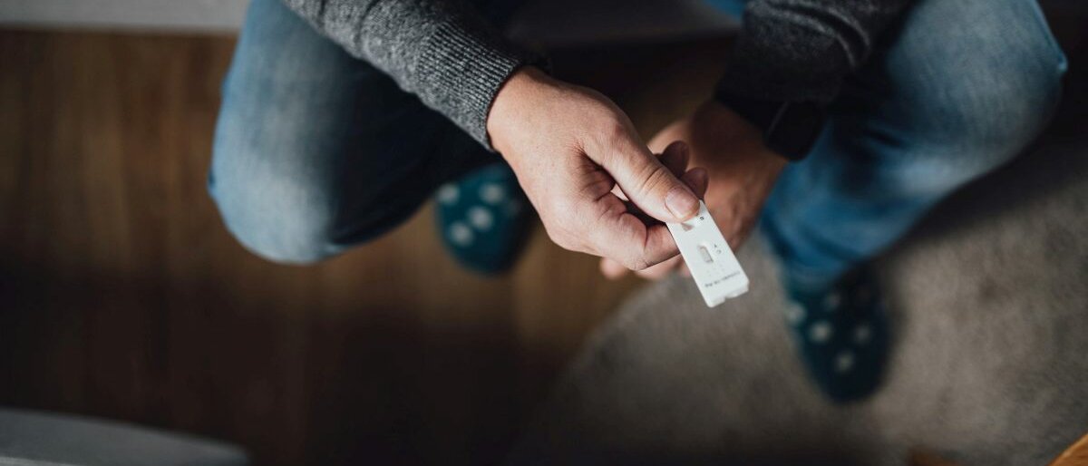 Selbsttest Ein Mann, der auf einer Couch sitzt und einen Corona-Selbsttest in den Händen hält.