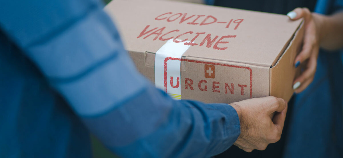 Eine Person übergibt einer anderen einen Karton mit der Aufschrift "Covid-19 Vaccine Urgent".