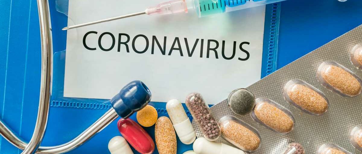 Auf einem blauen Ordner mit der Aufschrift "Coronavirus" liegen verschiedene Tabletten und Kapseln, eine Spritze und ein Stethoskop.