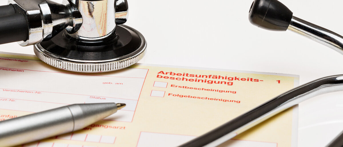 Krankschreibung Eine Arbeitsunfähigkeitsbescheinigung liegt auf dem Schreibtisch neben einem Stift und einem Stethoskop