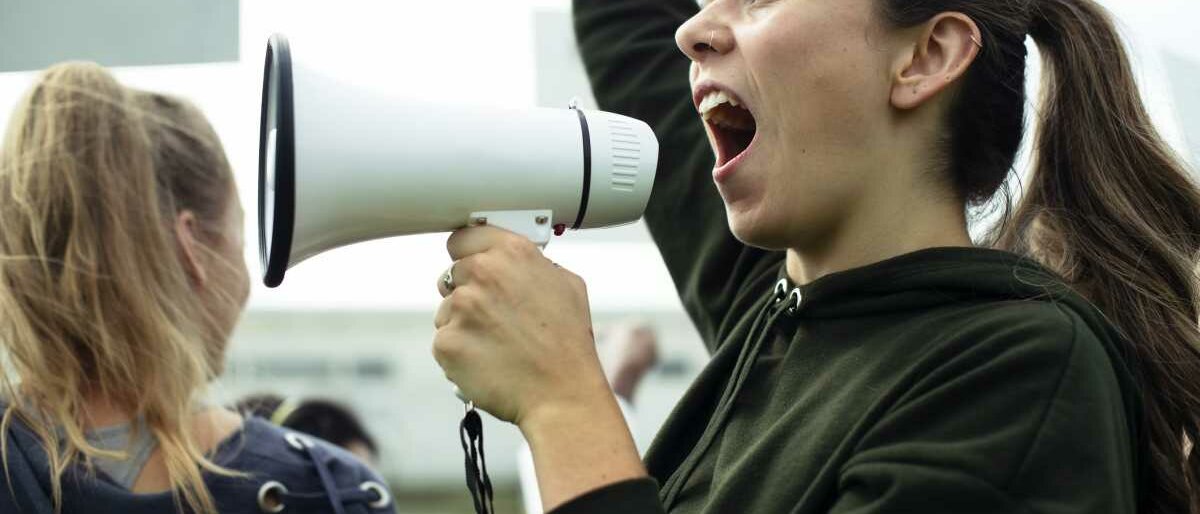 Eine junge Aktivistin schreit in ein Megafon.