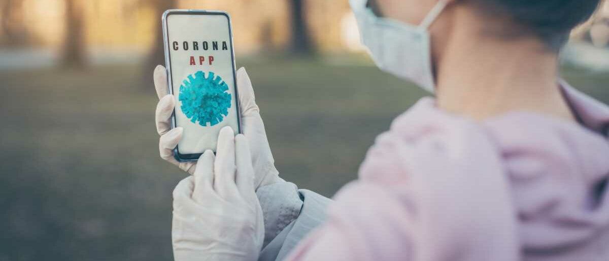 Eine ältere Frau, die Mundschutz und Handschuhe trägt, nutzt auf ihrem Smartphone eine Corona-App.