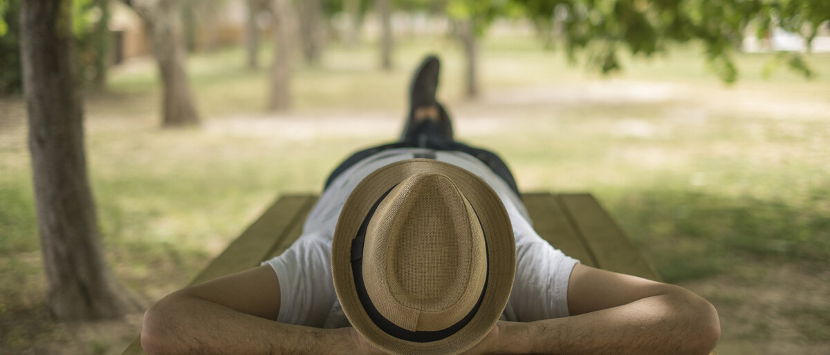 Ein Mann schläft im Schatten unter einem Baum mit seinem Strohhut über dem Gesicht.