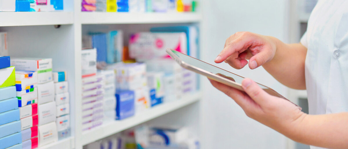 Ein Apothekenmitarbeiter mit Tablet kontrolliert die Arzneimittelbestände