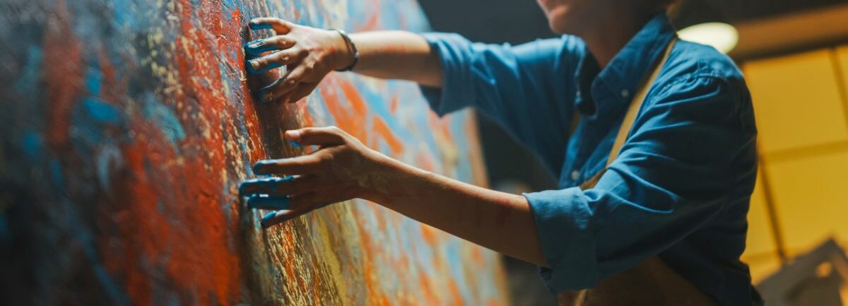 Eine Frau malt mit ihren Händen ein abstraktes Bild in vielen Farben.