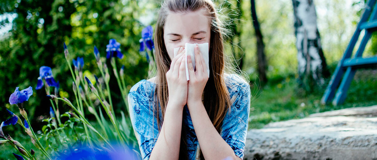 Eine junge Frau sitzt auf einer Blumenwiese und niest.