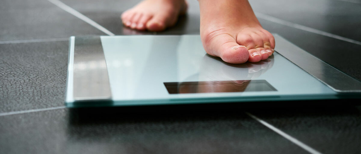 Ein unbekleideter Fuß tritt vorsichtig auf eine digitale Personenwaage