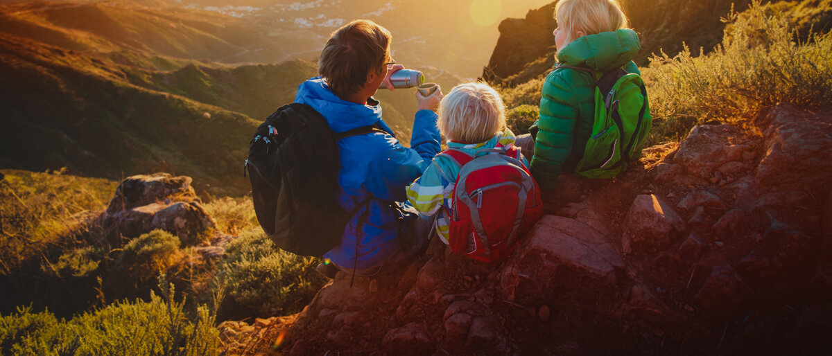 Bergwandern Ein Vater und zwei Kinder machen eine Wanderpause in den Bergen.