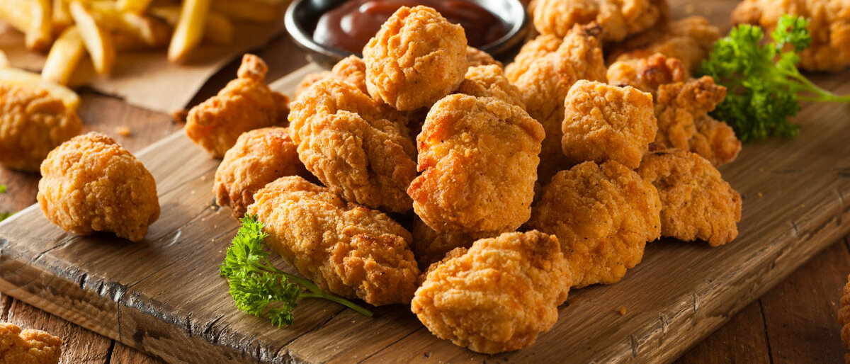 knusprige Chicken Nuggets, Pommes und ein Ketchupschälchen auf einem Holzbrett