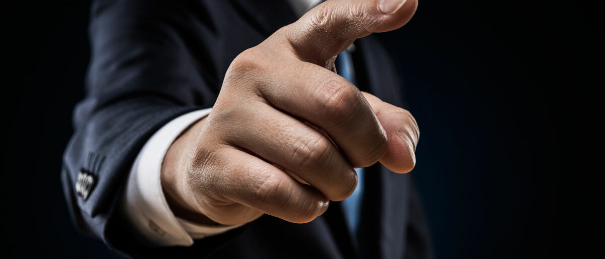 Ein Mann im Anzug zeigt mit ausgestrecktem Finger drohend auf den Betrachter.