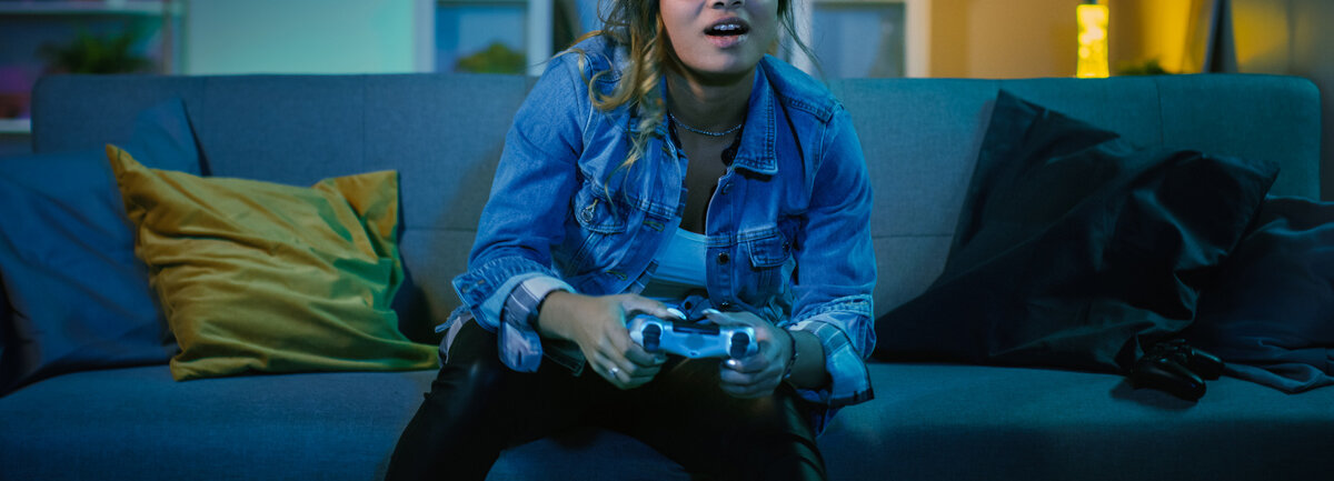 Eine junge Frau sitzt auf einer Couch und spielt ein Videospiel.