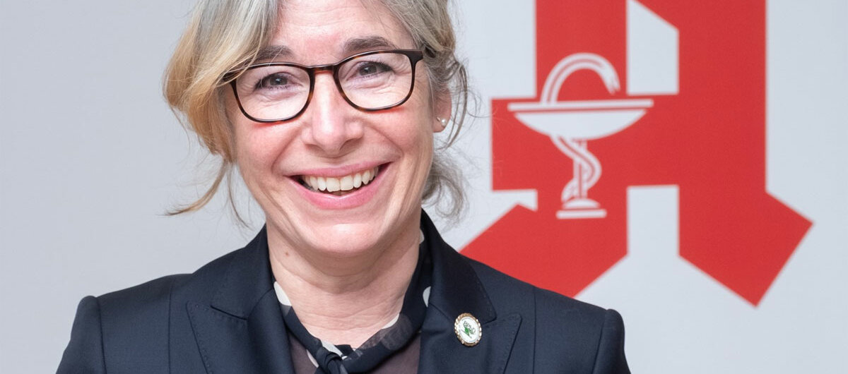 Gabriele Regina Overwiening lächelt, im Hintergrund sieht man das Apotheken-A.