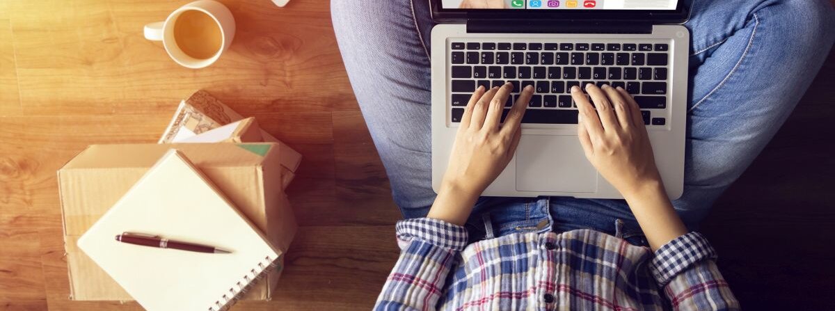 Jemand sitzt mit einem Laptop in den Händen im Schneidersitz.