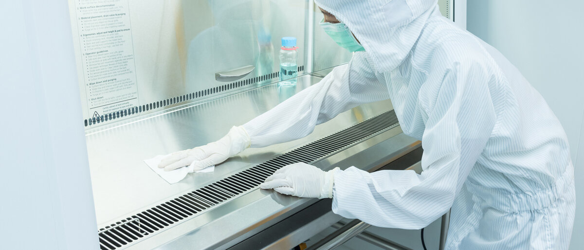 Eine Person in Schutzausrüstung desinfiziert eine Laminar Air Flow Box.