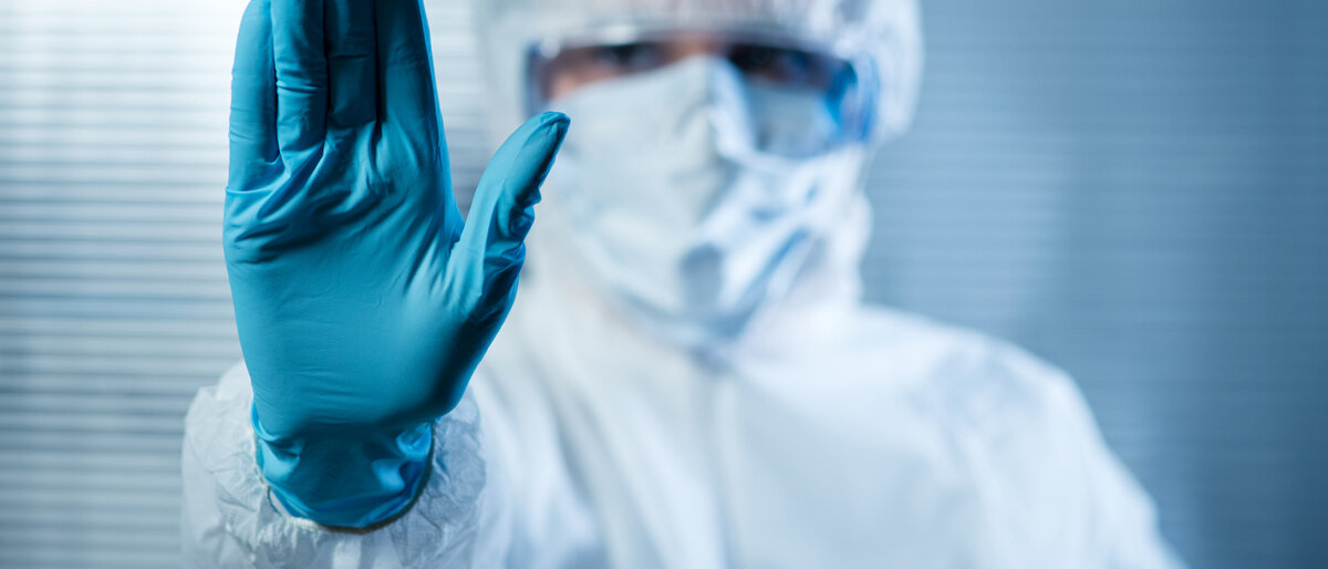 Ein Wissenschaftler im Schutzanzug hält eine behandschuhte Hand vor und signalisiert so "Stopp!".