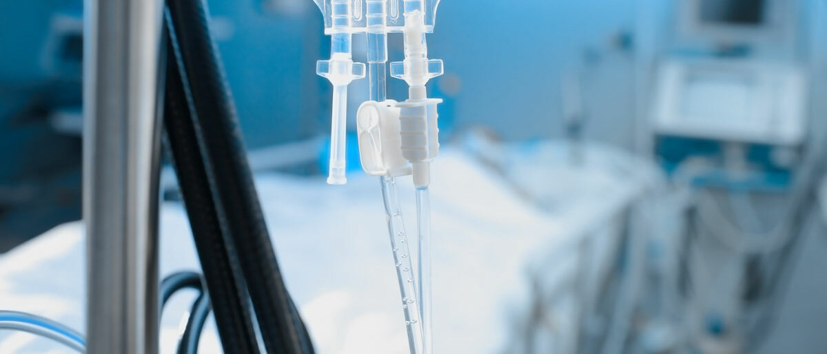 Eine Infusionslösung, im Hintergrund ein Krankenbett