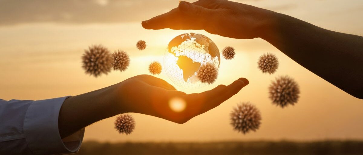 Welt Zwei Hände die eine schwebende grafische Weltkugel umschließen. Von außen versuchen Coronaviren einzudringen.