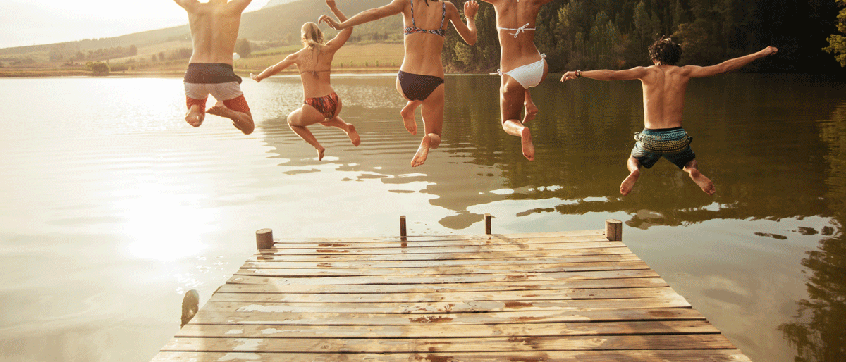 Eine Gruppe Jugendlicher springt in einen Badesee.