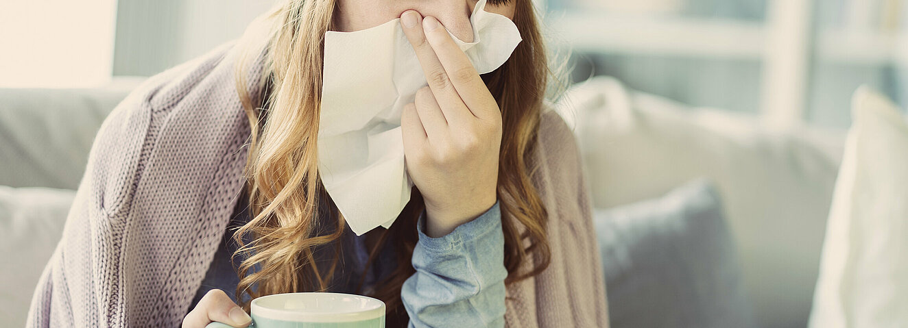Eine Frau putzt sich die Nase mit einem Papiertaschentuch.