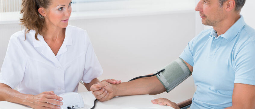 Apothekerin misst Blutdruck eines Kunden mit einem Oberarm-Blutdruckmessgerät