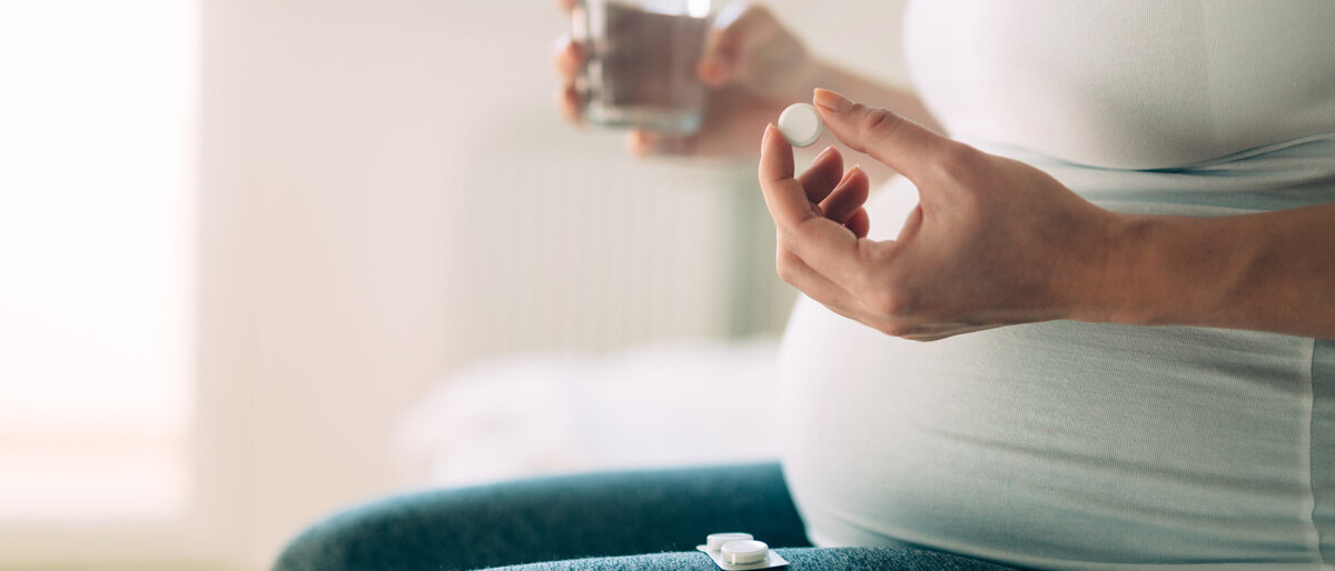 Eine schwangere Frau hält eine Tablette und ein Glas Wasser in der Hand.