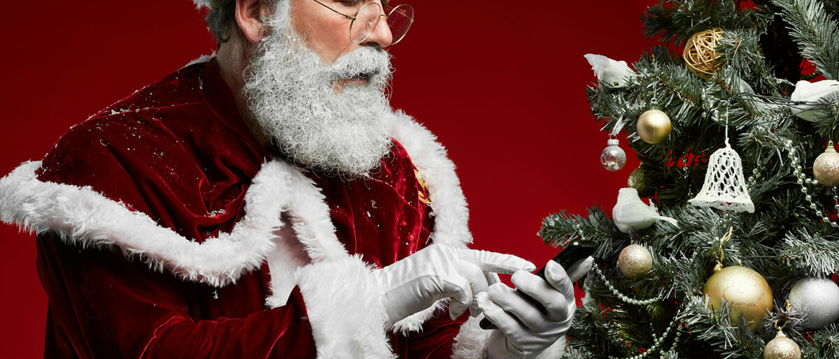 Weihnachtsmann Der Weihnachtsmann schaut auf sein Smartphone.