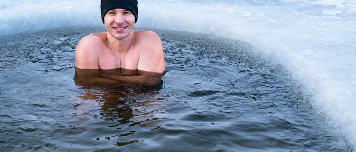 lächelnde Ein Mann mit Mütze steht im Winter im kalten Wasser.